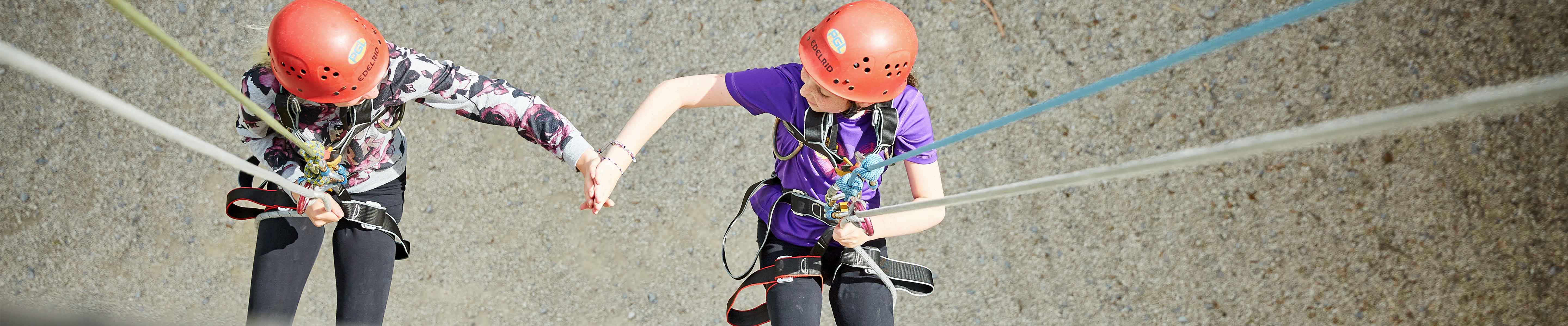 Two girls on an abseil wall giving each other a high five